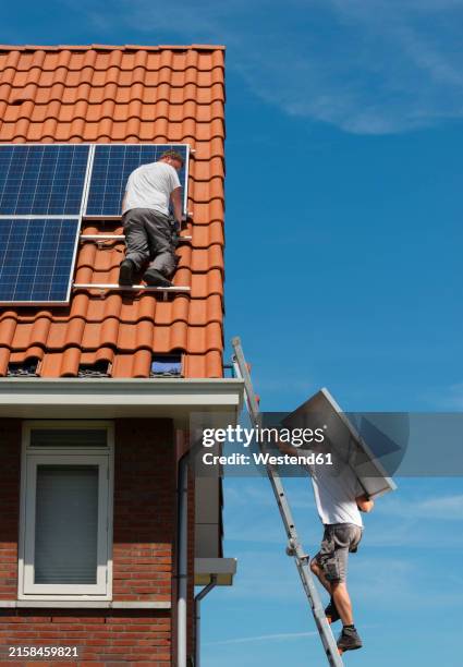 engineers installing solar panels on roof under blue sky - zonnepanelen stockfoto's en -beelden