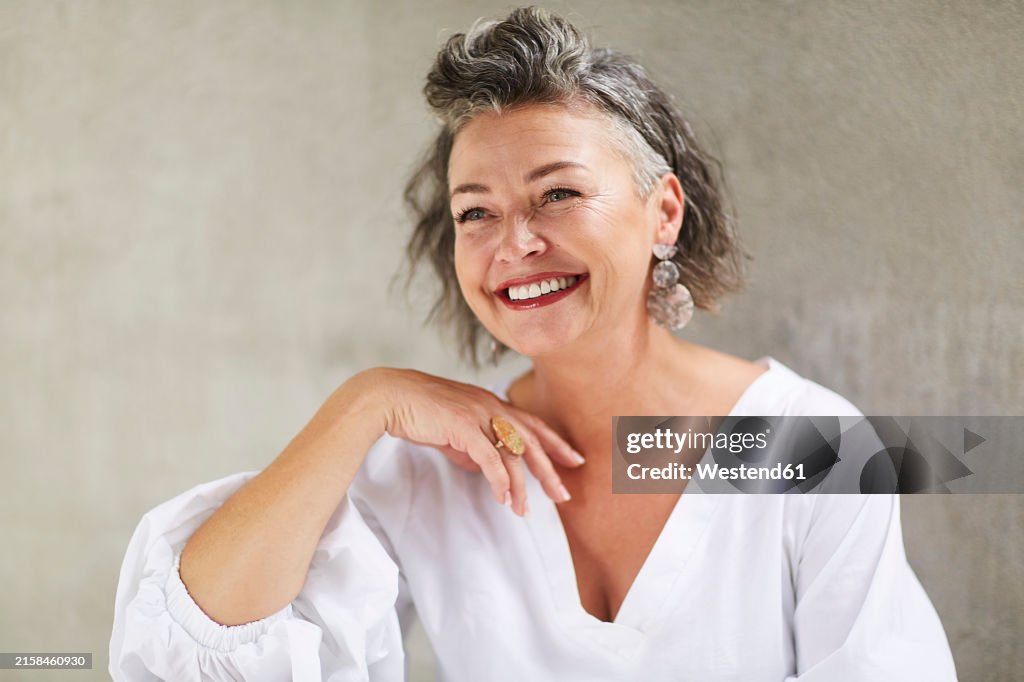 Happy mature woman sitting in front of gray wall