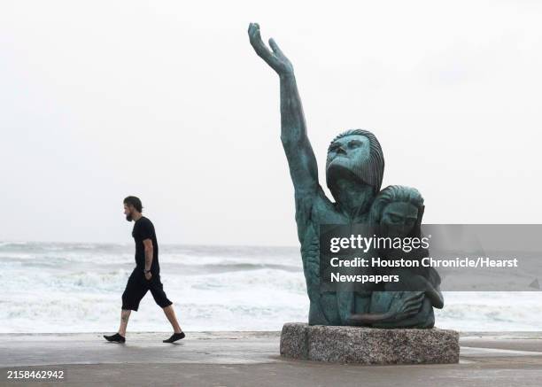 Waves crash along the seawall as a man passes the 1900 storm memorial while rain rolls in, Wednesday, June 19 in Galveston, Texas. The statue honors...