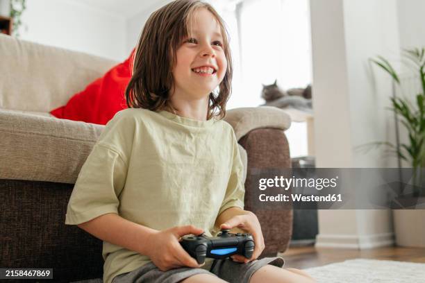 smiling boy sitting and playing video game at home - solo bambini maschi foto e immagini stock