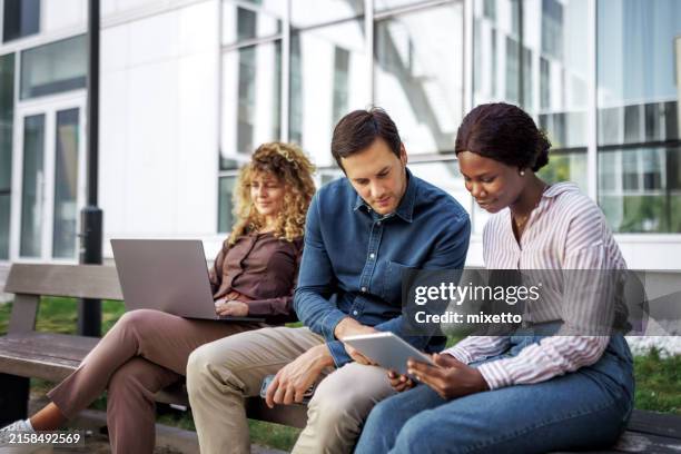young casually clothed business people using laptop and digital tablet while sitting on a bench in front of modern company - bring your own device stock pictures, royalty-free photos & images