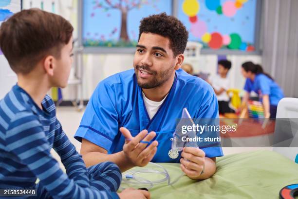 male paediatric nurse explaining mask to child patient - enfermeiro imagens e fotografias de stock