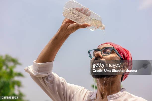 heat wave: a close-up of a young man pouring water from a plastic bottle on his face during a hot afternoon while traveling. - heat wave india stock pictures, royalty-free photos & images
