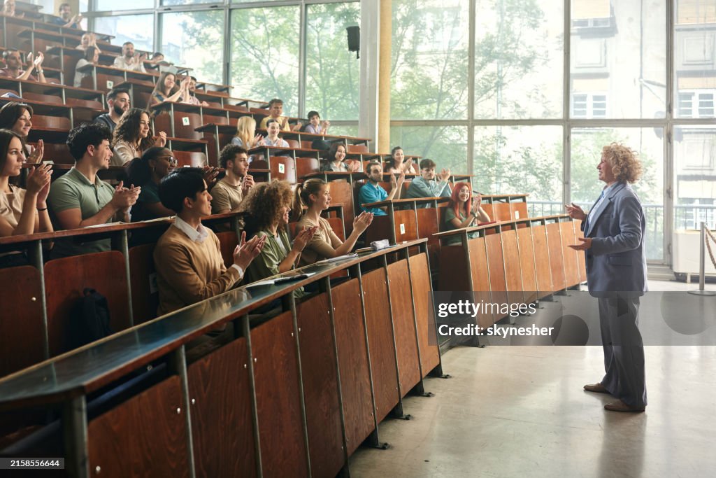 Crowd of happy students applauding to their professor in amphitheater.