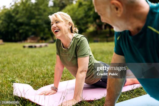 mature couple in sports clothes exercising in nature - yoga outdoors stock pictures, royalty-free photos & images