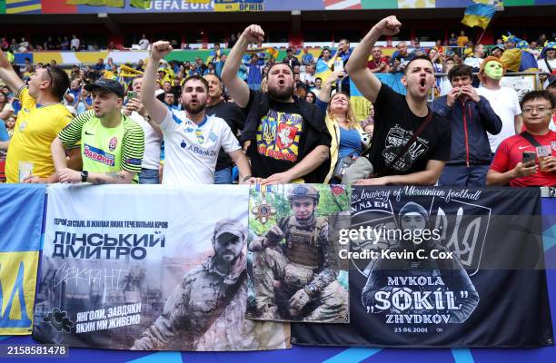 Fans of Ukraine show their support as a flag showing a tribute to Mykola Zhydkov is displayed prior to the UEFA EURO 2024 group stage match between...