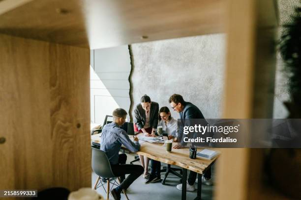 four colleagues sitting on the table in the office - immobilienbüro stock-fotos und bilder