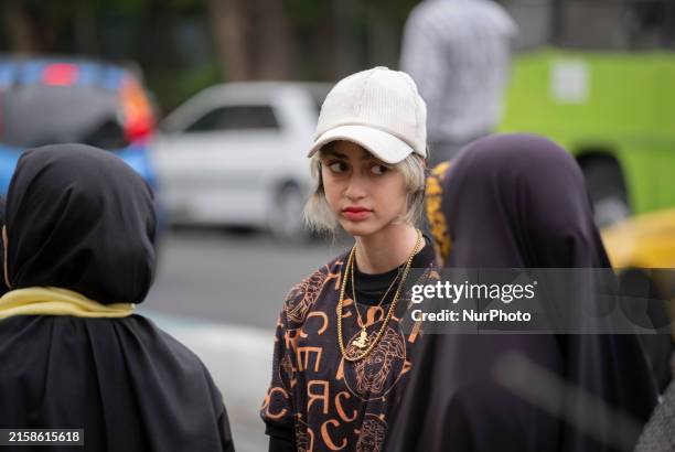 Young Iranian woman, who is not wearing a mandatory headscarf, is standing with two veiled women outside a sports hall during an electoral campaign...