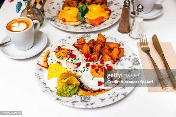 huevos rancheros fried eggs served for breakfast with roasted potatoes and guacamole - huevos-rancheros fotografías e imágenes de stock