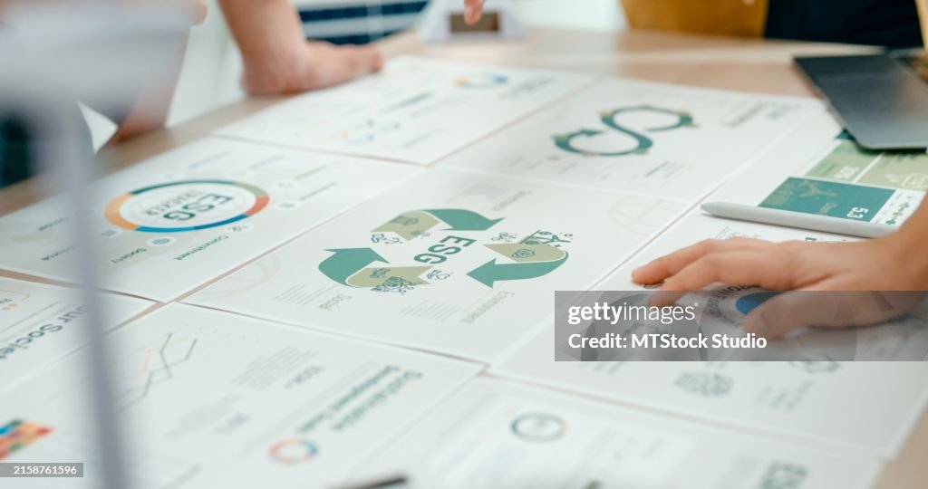 Closeup of team members examine ESG-related documents, pointing and discussing investment strategies for sustainable and renewable energy resources. Eco-Friendly Business Discussing ESG Goals.
