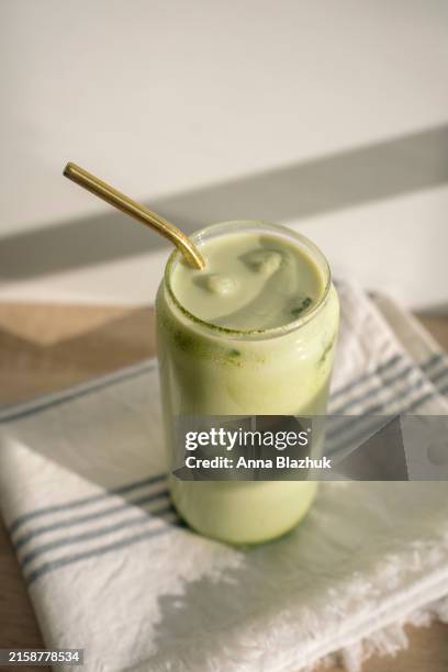 glass of iced matcha latte on table in bright sunlight. cold summer drink made of green tea ice cubes and milk. - eiswürfel stock-fotos und bilder
