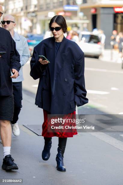 Guest wears navy oversized blazer, red checkered skirt outside Sacai during Menswear Spring/Summer 2025 as part of Paris Fashion Week on June 23,...