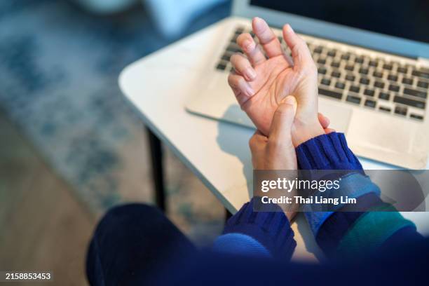 image recadrée d’une femme asiatique massant sa main et son poignet arthritiques après de longues heures devant un ordinateur, indiquant des douleurs et des rhumatismes. - poignet photos et images de collection