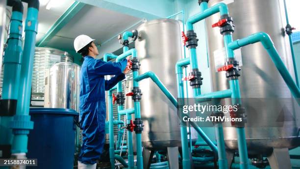 ingeniero de mantenimiento trabajador con casco de seguridad ajustando válvulas y examinando el manómetro de las tuberías industriales en una instalación de tratamiento de agua. embotellado de agua - planta de agua fotografías e imágenes de stock