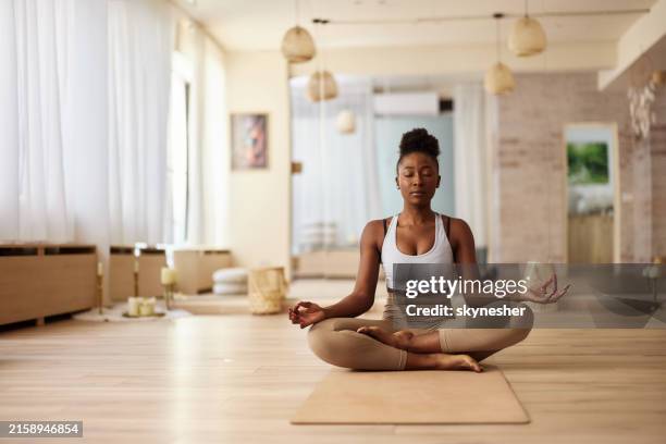 femme afro-américaine méditant en position de lotus au studio de yoga. - méditer photos et images de collection