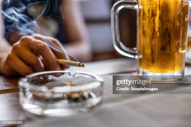 the hand of a smoking man or woman on a table led an ashtray with draft beer in a pub. - produto relacionado com tabaco - fotografias e filmes do acervo