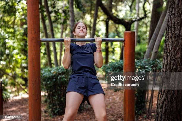 teenage girl exercising in nature park, doing chin-ups on horizontal bar in outdoor gym - girls in pull ups stock pictures, royalty-free photos & images