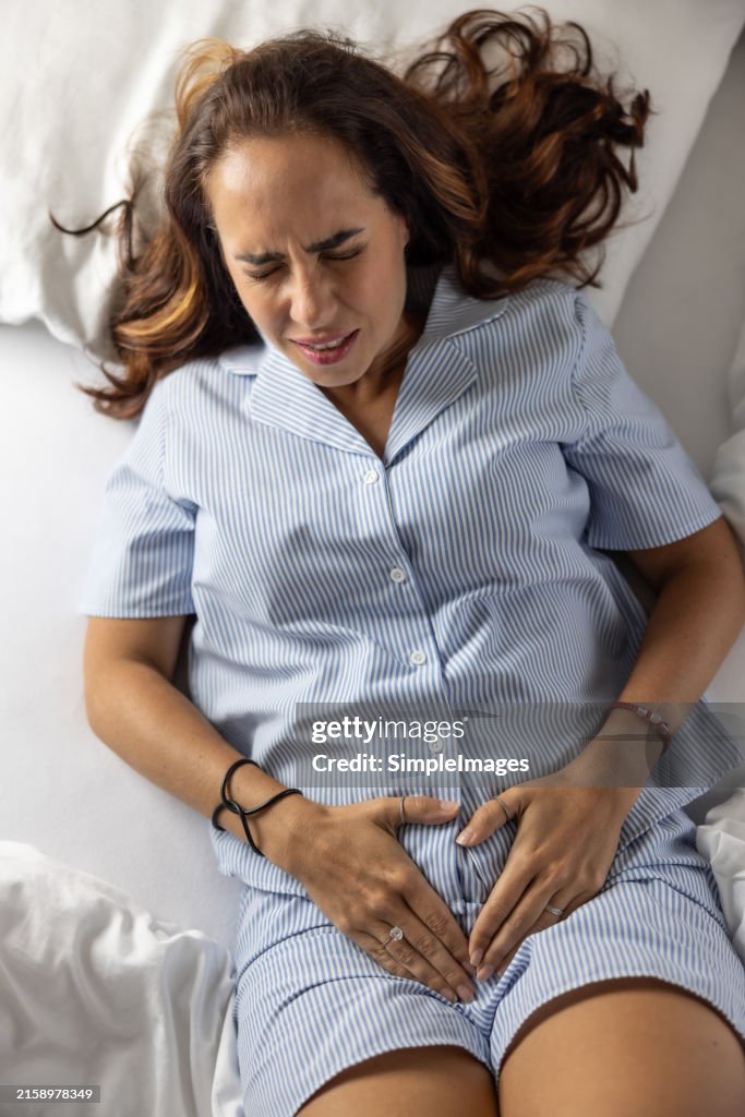 A young woman suffers from menstrual pains,lying on the bed. In spasms, he holds his crotch area.