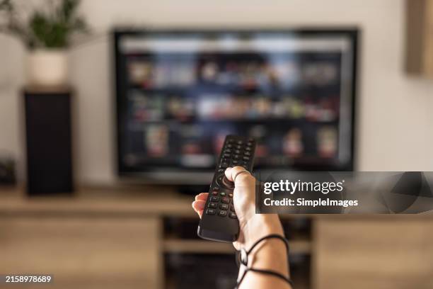 a woman is holding a remote control of a smart tv in his hand. in the background you can see the television screen with streaming entertainment apps for video on demand. - fernsehen stock-fotos und bilder