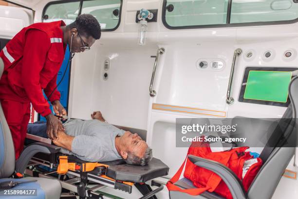 paramedic checking pulse of senior man lying on stretcher in ambulance - stretcher stock pictures, royalty-free photos & images