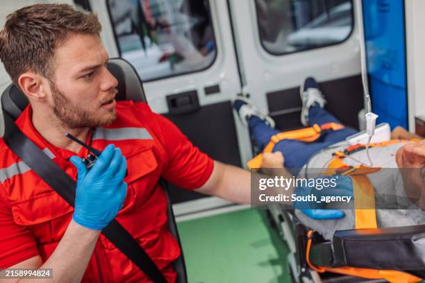 sanitäter spricht über funk während des transports eines patienten im krankenwagen - intensivmedizin stock-fotos und bilder