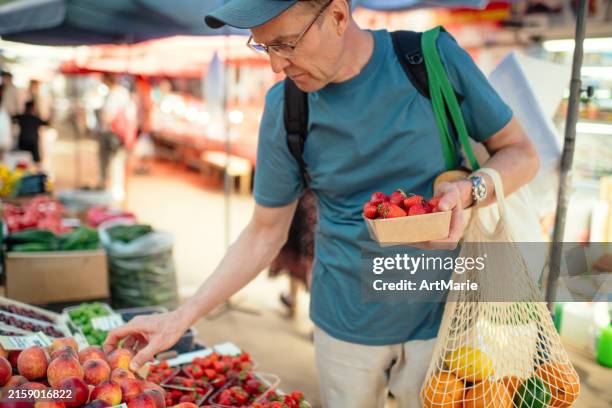 manos de hombre mayor con bolsa de compras reutilizable que elige fresa en un mercado de agricultores, concepto de conservación del medio ambiente y sostenibilidad - puesto de mercado agrícola fotografías e imágenes de stock