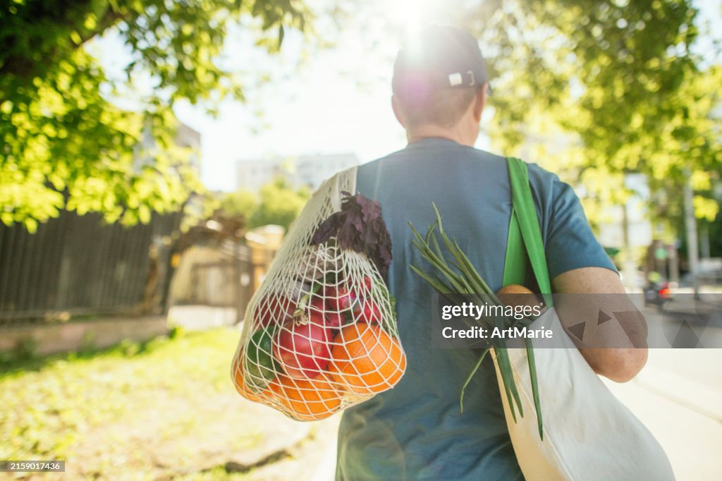 Homem idoso carregando frutas e legumes em saco de compras reutilizável e saco de malha, conceito de conservação ambiental e sustentabilidade