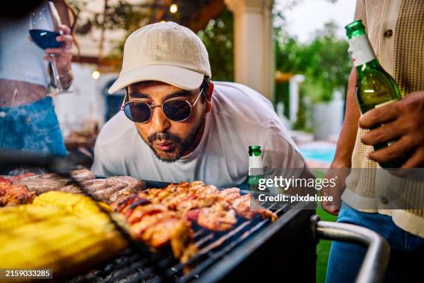 man getting the bbq or grill, fired up by blowing on the coals. outdoor social gathering. summer cooking and food concept. - utegrillat bildbanksfoton och bilder