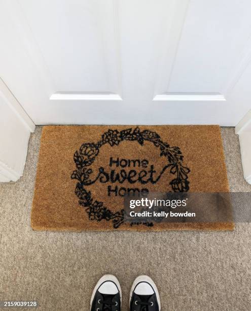 first time buyer standing in front of a doorway mat that says home sweet home - zerbino foto e immagini stock