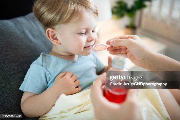 madre che dà lo sciroppo per la tosse al suo figlioletto a casa. - sciroppo foto e immagini stock