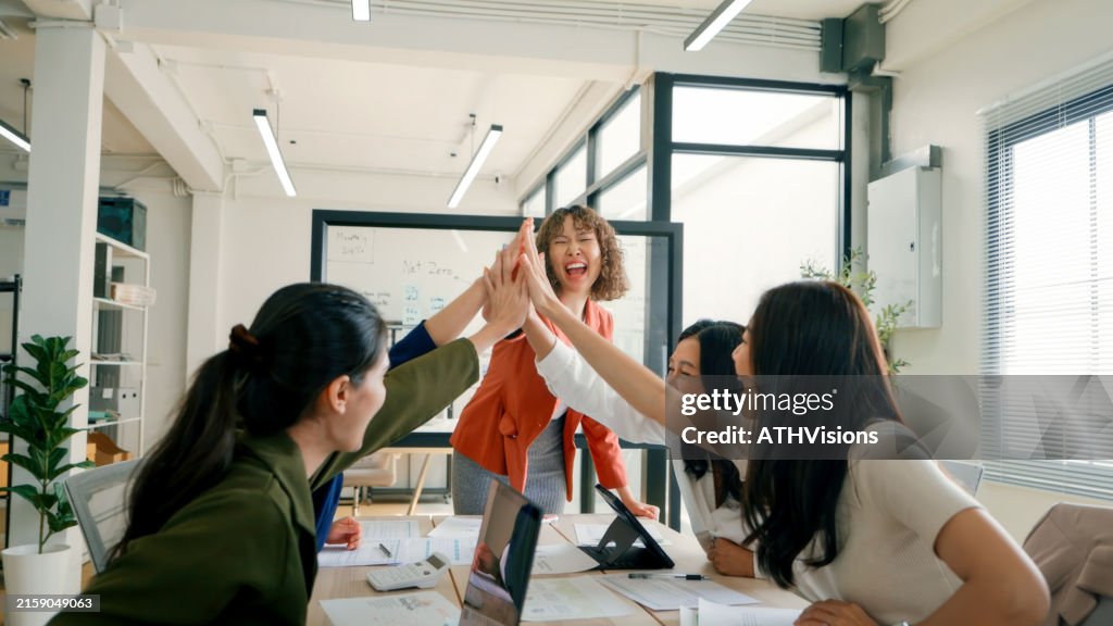 Ein vielfältiges Team von Geschäftsleuten feiert mit einem High-Five während eines ESG-Meetings (Environmental, Social, and Governance) in einer hellen, modernen Büroumgebung.