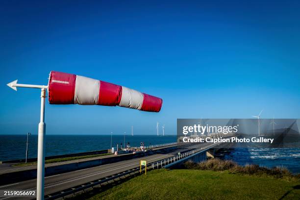 a windsock flutters vibrantly in the breeze beside a coastal road and wind turbines - windsock stock pictures, royalty-free photos & images