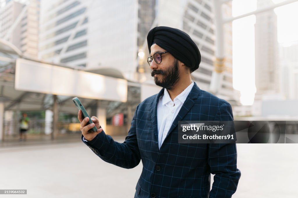 Un homme d’affaires indien lisant un SMS sur un smartphone debout dans la rue de la ville