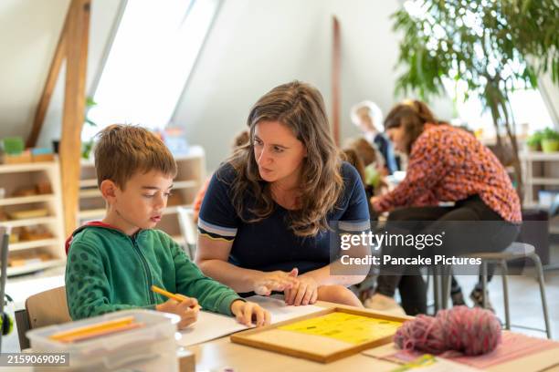 a teacher assists a young boy with his schoolwork in a bright classroom setting - showing stock pictures, royalty-free photos & images