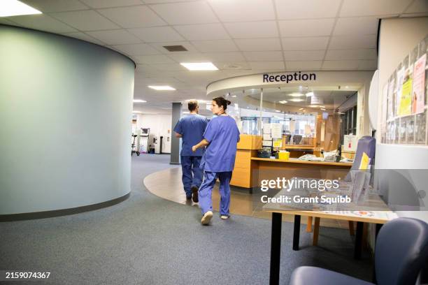 two healthcare professionals walking towards a reception area of a medical practice - hospital interior signage stock pictures, royalty-free photos & images