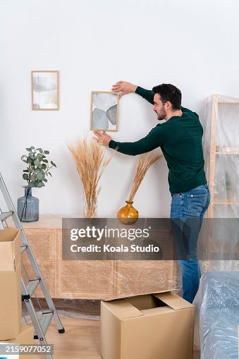 Man arranging a picture frame in a room with moving boxes Man arranging a picture frame in a room with moving boxes