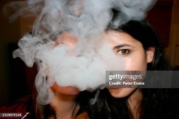 a young woman is exhaling a large cloud of smoke, obscuring the upper part of her face. one eye is visible, and she has dark hair - cigarette électronique photos et images de collection