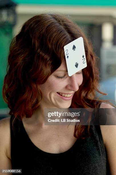 a smiling woman with red hair has a playing card, the two of spades, stuck to her forehead - dois de espadas imagens e fotografias de stock