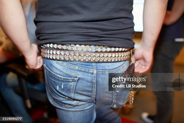 a close-up view of a person wearing blue denim jeans and a black shirt tucked in, with a studded belt and keychain accessory attached to a belt loop - belt stock pictures, royalty-free photos & images