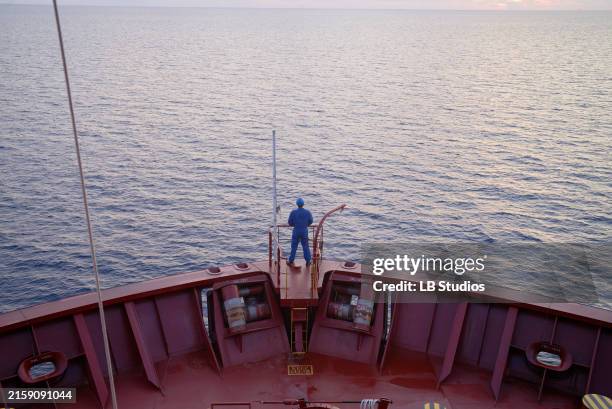 a person stands on the bow of a red ship, gazing out at the calm blue sea during sunset - boat stock pictures, royalty-free photos & images