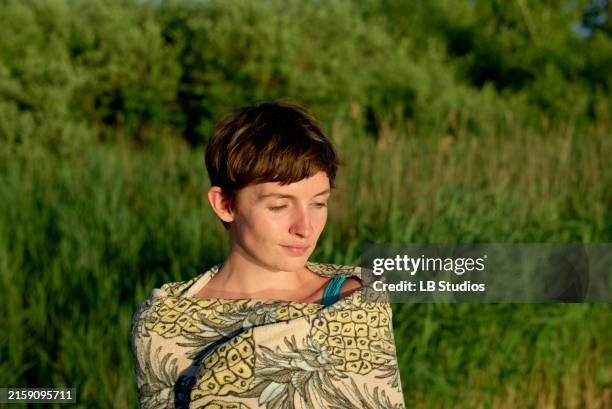 a young woman with a pixie haircut is outdoors with eyes closed and a calm expression, bathed in soft sunlight with green foliage in the background - pixie cut stock pictures, royalty-free photos & images