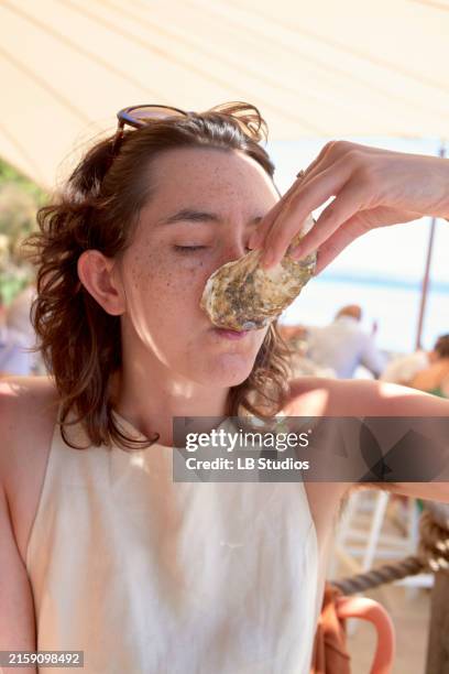 a woman is eating an oyster at a seaside restaurant - gouter photos et images de collection