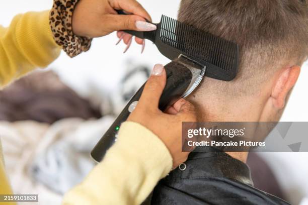 a person is receiving a haircut from a hairstylist using electric clippers and a comb - man fashion haircut stock pictures, royalty-free photos & images