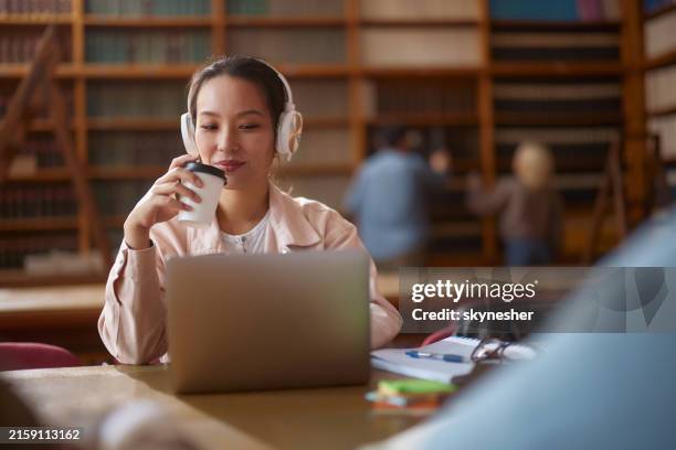 smiling chinese student having an online class over laptop in library. - zoom classroom stock pictures, royalty-free photos & images