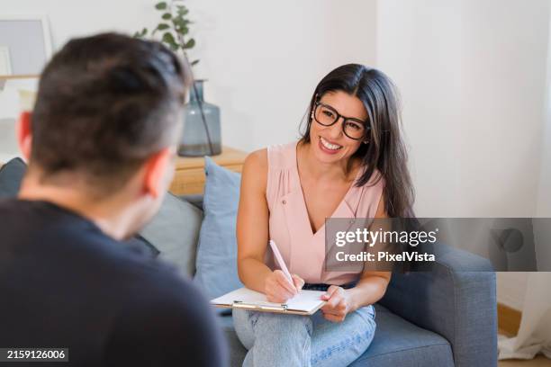 psicologo sorridente che prende appunti durante la sessione di terapia con paziente maschio - lettino-dello-psicoanalista foto e immagini stock