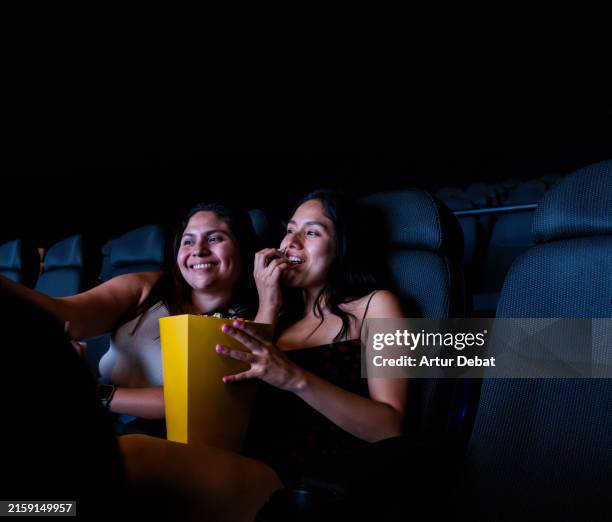 latin women watching a movie together taking a selfie at the cinema - industria cinematográfica fotografías e imágenes de stock