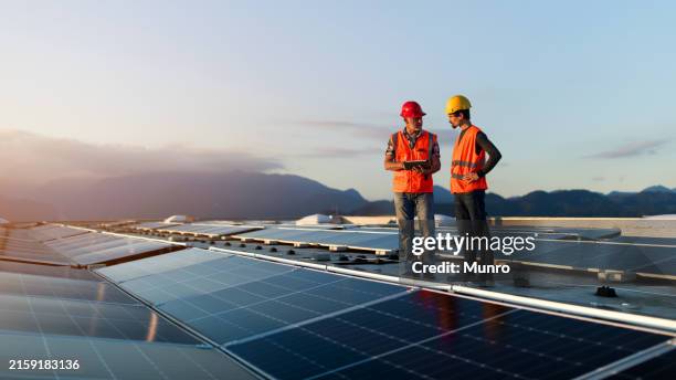 tecnici in giubbotti riflettenti che controllano l'impianto solare installato sul tetto dell'edificio - energia sostenibile foto e immagini stock