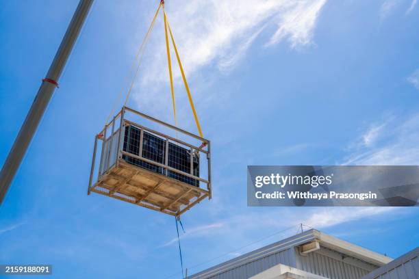 a crane is carrying solar panels onto the factory roof for installation. - battery life stock pictures, royalty-free photos & images