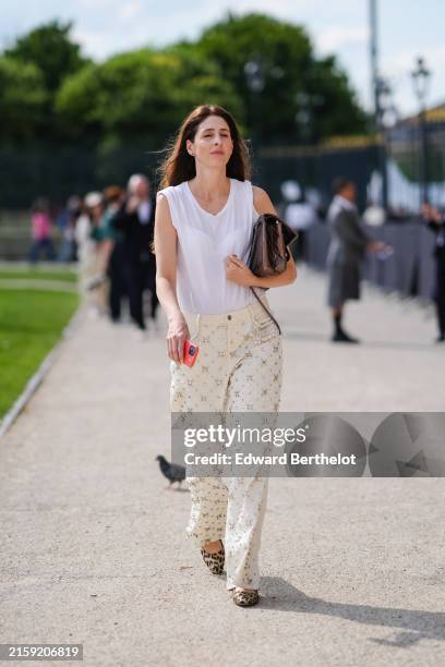 Guest wears white sleeveless sheer mesh shirt, shiny dark brown quilted leather bag, cream loose denim jean pants with silver embroidery pattern,...