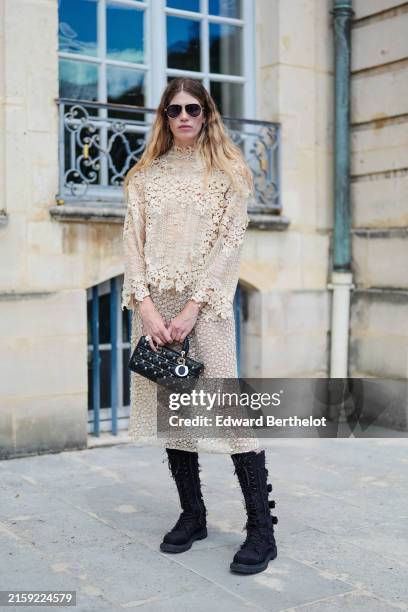 Veronika Heilbrunner wears black sunglasses, silver hoop earrings, cream lace pattern long sleeve shirt, gold bracelets, silver rings, shiny black...